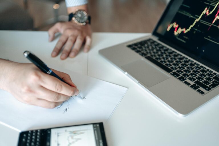 Hands analyzing financial data at a desk with a laptop and calculator.