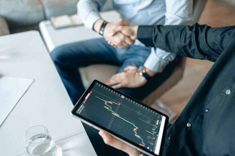 Two people shaking hands over a financial graph on a tablet, symbolizing a business agreement.